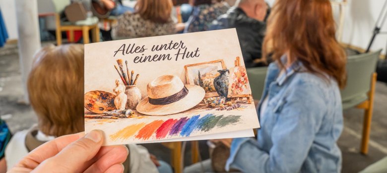 Ausstellung Alles unter einem Hut - Flyer im Vordergrund, Gäste und Musiker im Hintergrund
