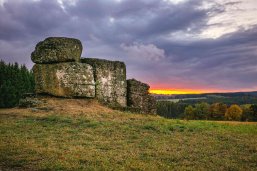 Der Ketzerstein, eine markante Basaltformation nahe Rennerod im Hohen Westerwald, erhebt sich auf 610 Metern Höhe. Anders als typische Basaltformationen, bei denen die Lava zu Säulen erstarrt, formte sie sich hier zu Blöcken. Diese geologische Besonderheit beeinflusst aufgrund des hohen Eisenanteils die Kompassnadel, was Wanderern ein einzigartiges Erlebnis bietet. Gut ausgeschilderte Wanderwege führen durch die idyllische Landschaft zu diesem Naturdenkmal, das sowohl geologisch Interessierte als auch Naturliebhaber begeistert. Der Ketzerstein, eine einzigartige Basaltformation nahe Rennerod im Hohen Westerwald, umgeben von Wanderwegen und malerischer Natur.