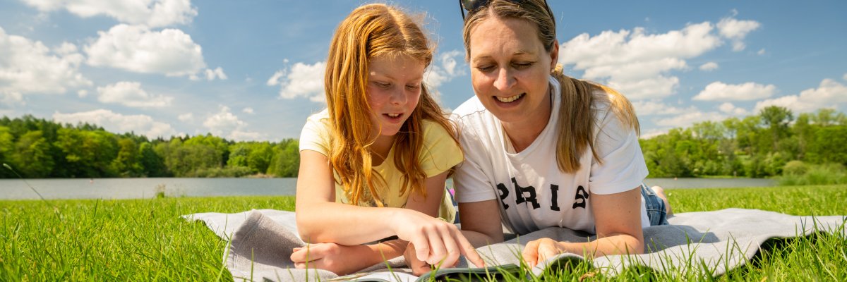 Mutter und Tochter liegen gemütlich auf einer Decke auf einer grünen Wiese beim Picknick an einem sonnigen Tag in der Nähe von Rennerod im Hohen Westerwald.