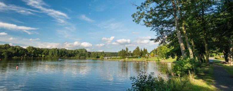 Der Secker Weiher in Rennerod, eingebettet im Hohen Westerwald, glänzt an Sommertagen mit seinem ruhigen, glitzernden Wasser und grünen Wiesen. Der Campingplatz am Ufer bietet Familien einen idealen Ort zum Entspannen, während Kinder am Wasser spielen. Die idyllische Atmosphäre macht den Weiher zu einem perfekten Ziel für erholsame Stunden in der Natur.